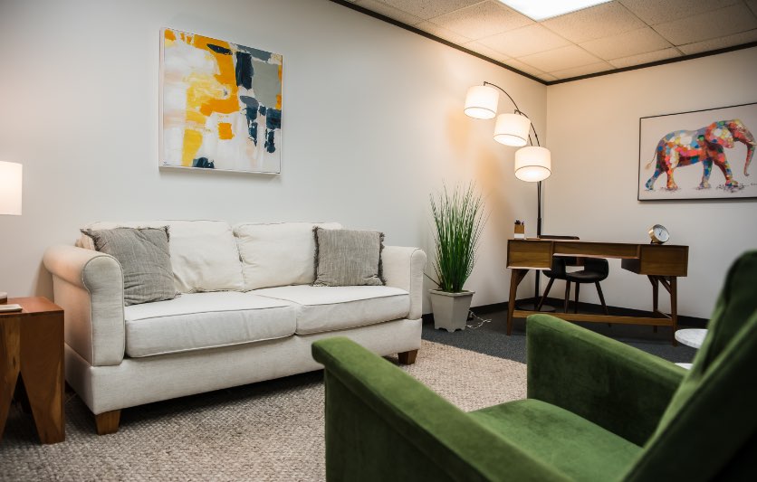 cream-couch-in-clinician-office-with-green-chair-and-mid-century-desk-in-corner